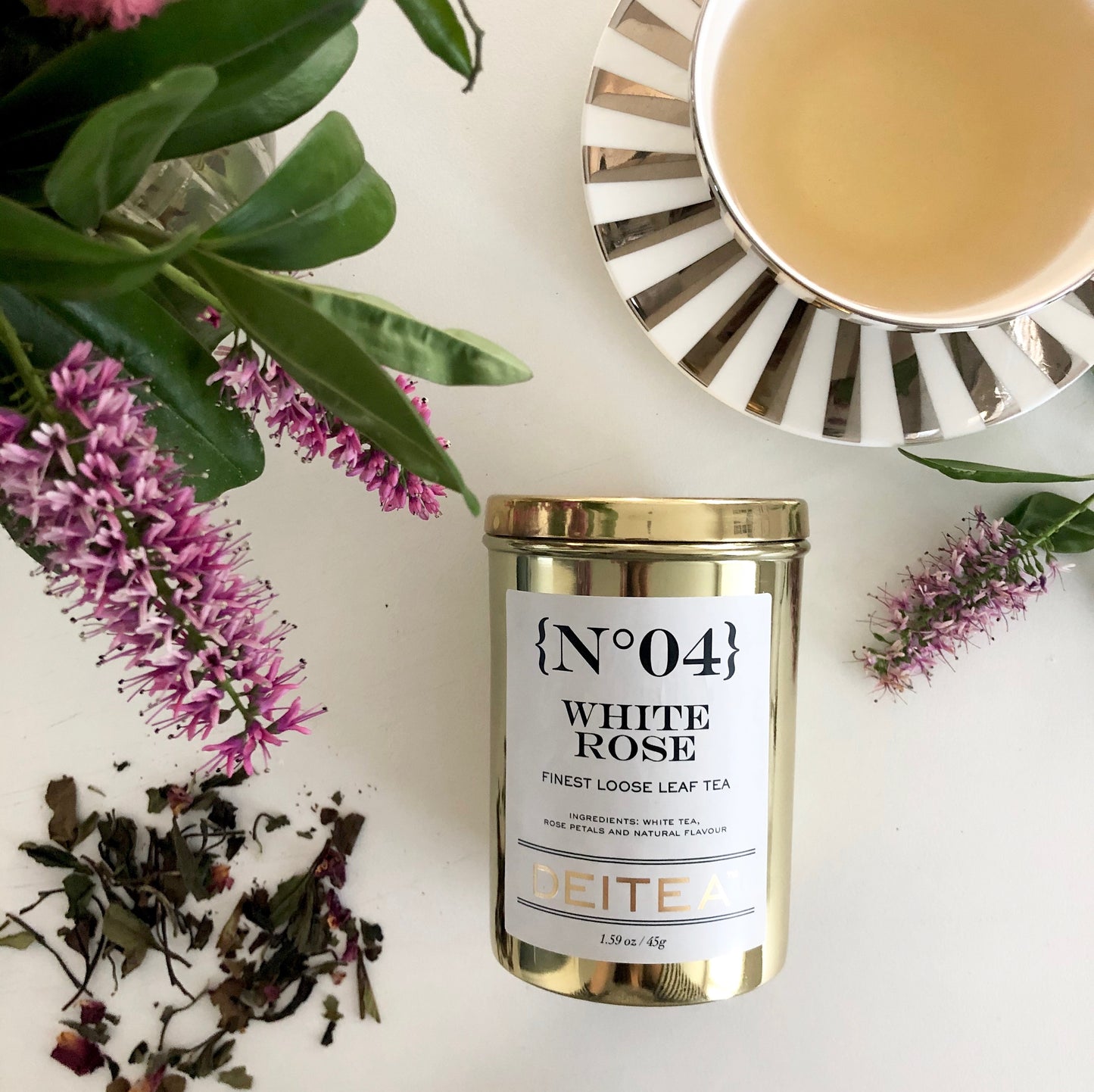 Pai mu tan white tea with rose petals scattered with a beautiful golden tea caddy and striped porcelain tea cup with elegant flowers